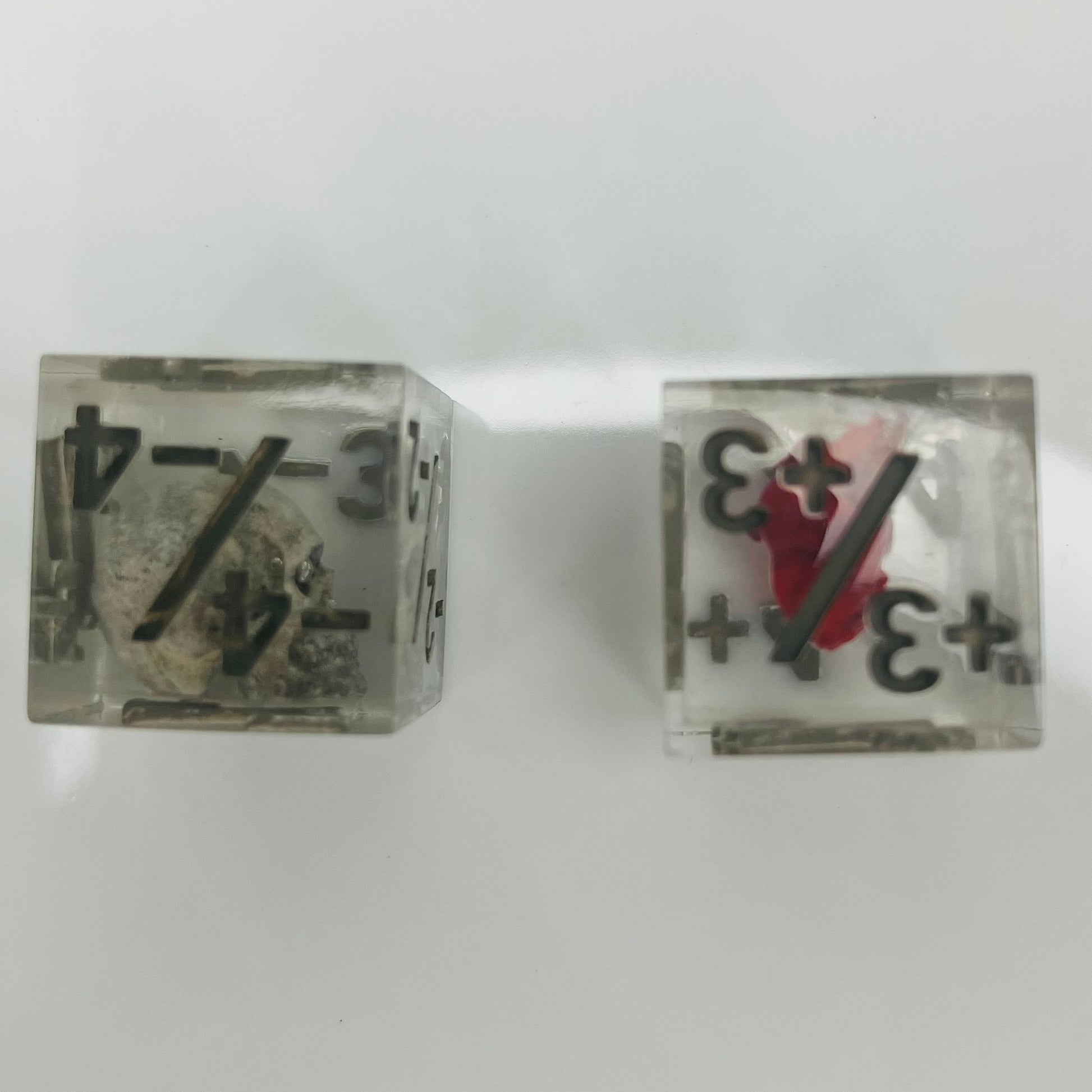 Two clear dice with black numbers with an embedded skull and heart