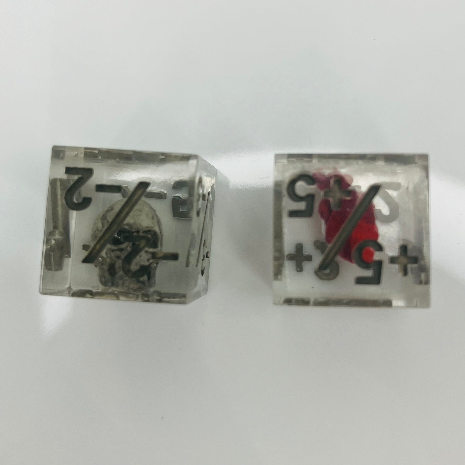Two clear dice with black numbers with an embedded skull and heart