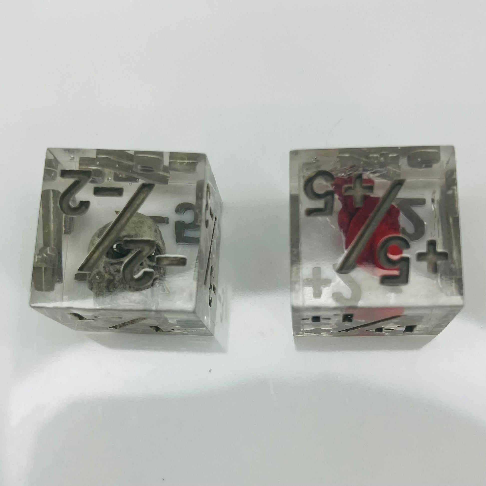 Two clear dice with black numbers with an embedded skull and heart